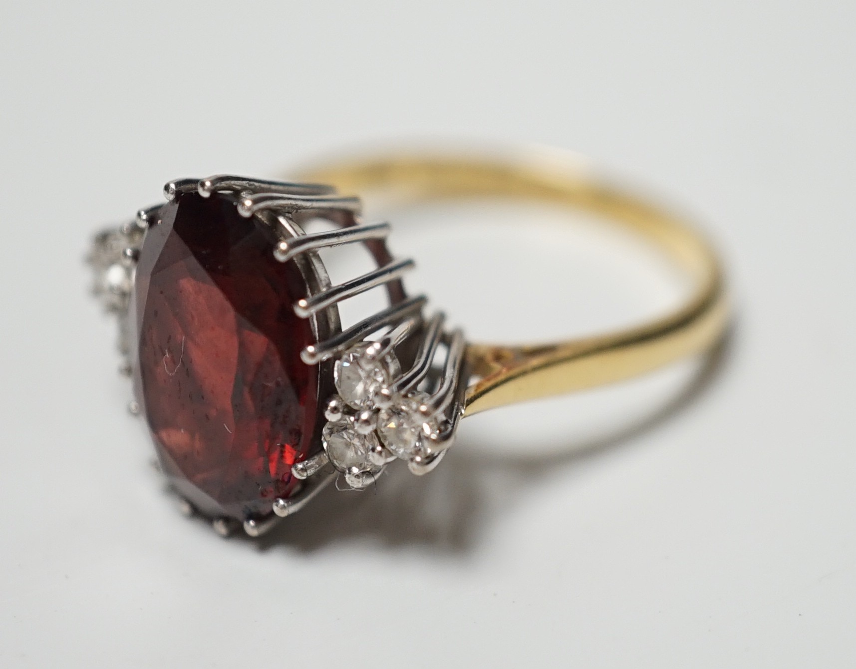 A modern 18ct gold and oval cut garnet set dress ring, with six stone diamond set shoulders, size M/N, gross weight 4.8 grams.